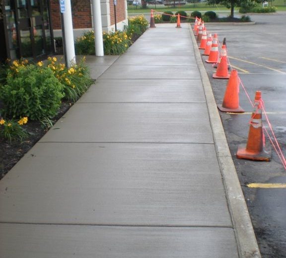 Wide concrete sidewalk pathway from a parking lot leading into a business