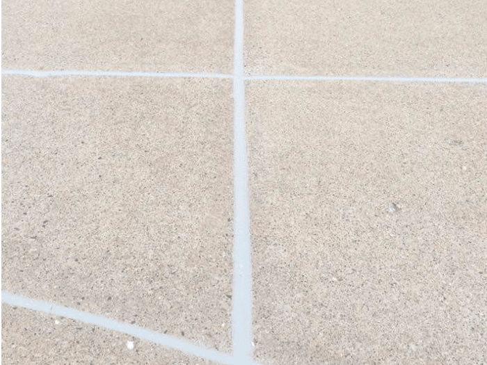 Close-up of a concrete driveway where the expansion joints have been freshly caulked. The caulking material is smooth and neatly applied, filling the gaps between the concrete slabs. The surrounding concrete is clean and appears recently resurfaced.