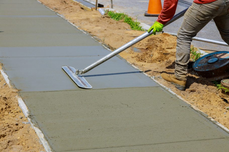 Worker smoothing out freshly poured concrete for a sidewalk