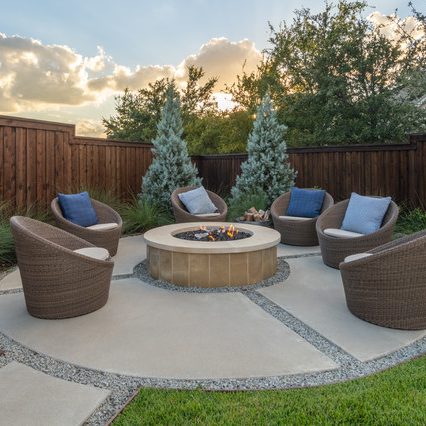 A circular designed custom patio with a central stone fire pit surrounded by modern wicker chairs