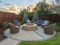 A circular designed custom patio with a central stone fire pit surrounded by modern wicker chairs
